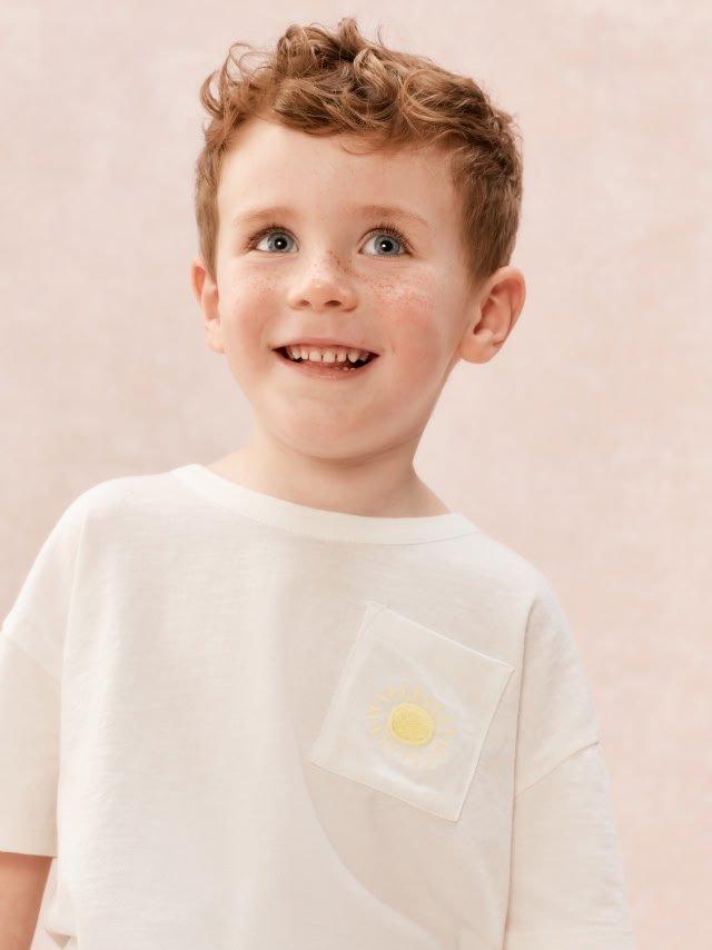 a young boy with a white shirt and a yellow sun on his shirt