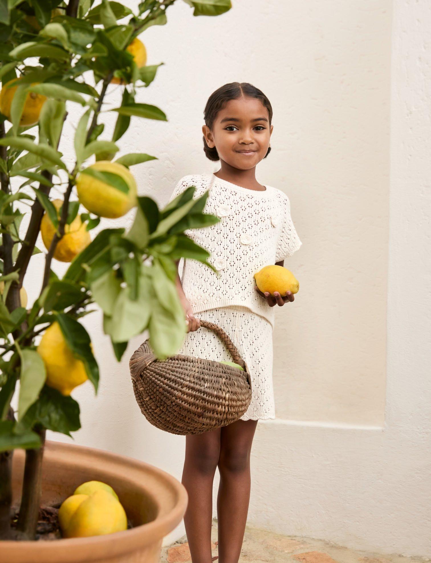 a young girl holding a basket of lemons and a potted plant