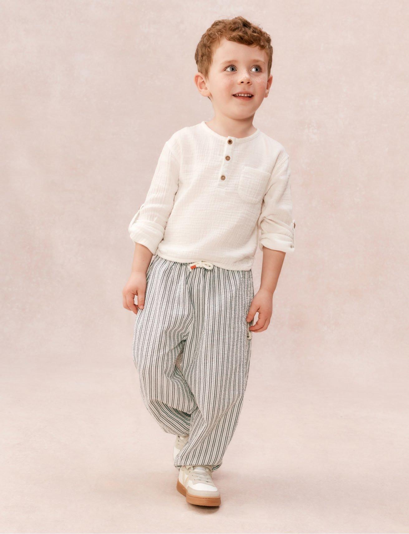 a young boy in a white shirt and striped pants