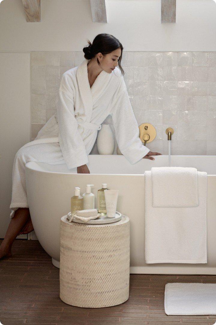 a woman in a white robe leaning over a bathtub