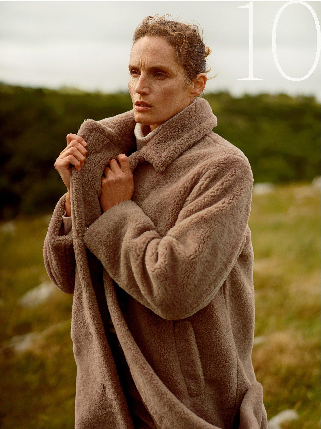 a woman in a brown coat standing in a field