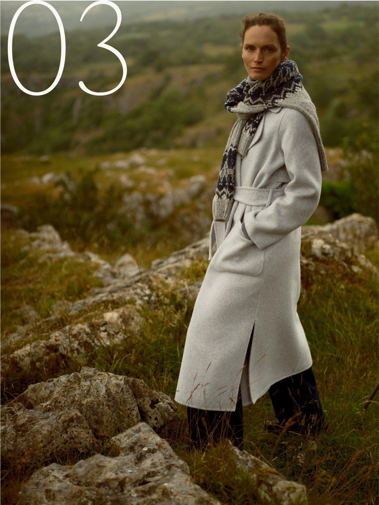 a woman in a long coat standing on a rocky hill