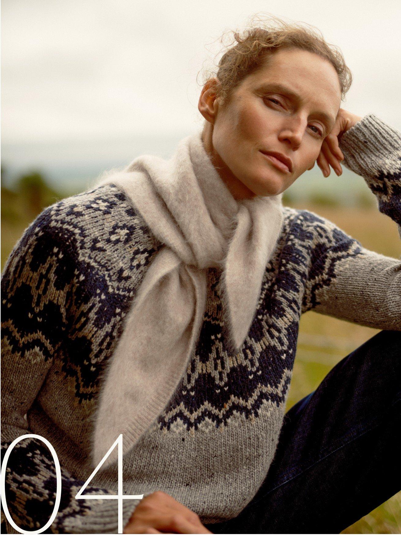 a woman in a sweater and scarf sitting on a bench