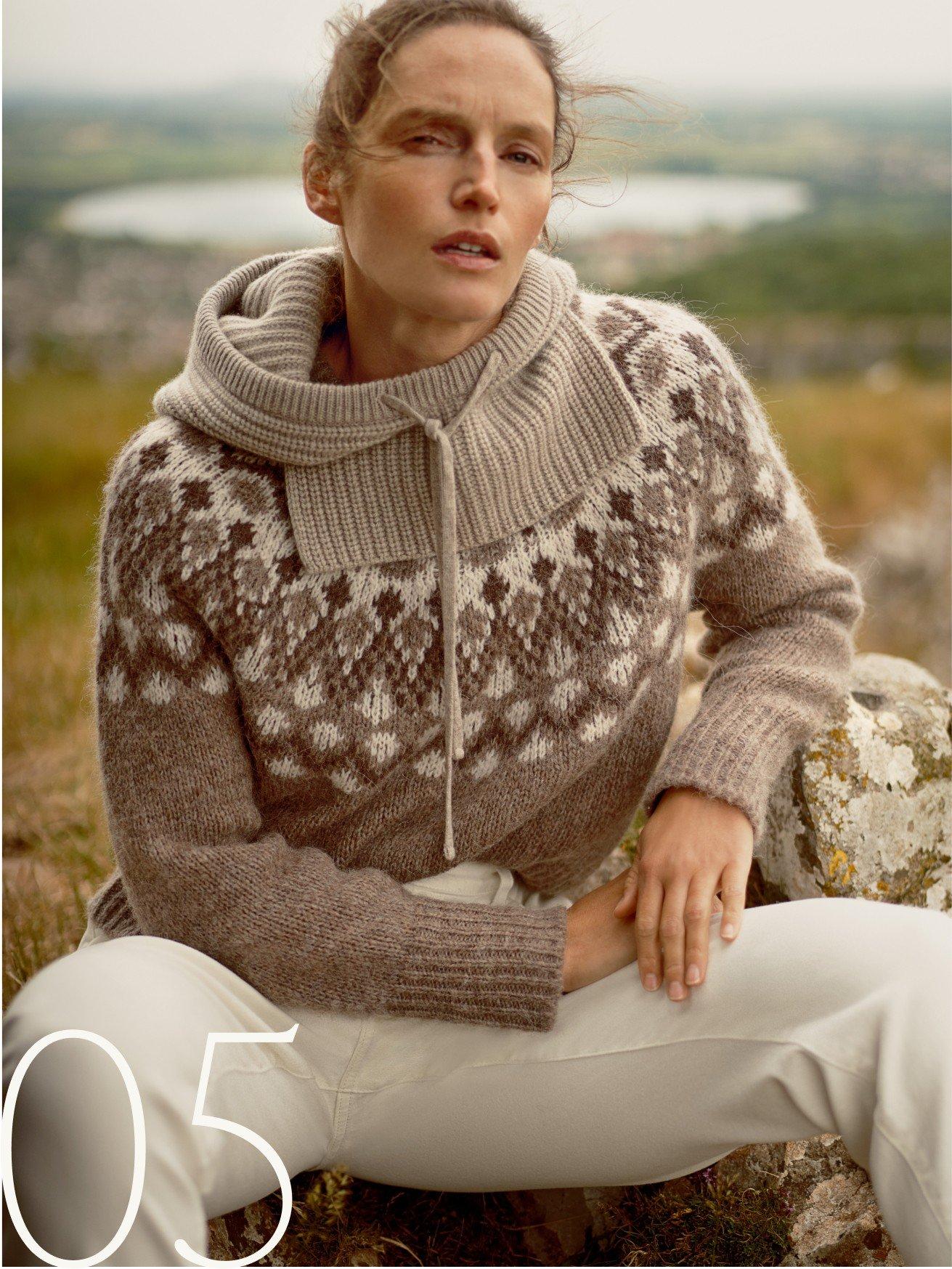 a woman in a sweater sitting on a rock with a bag