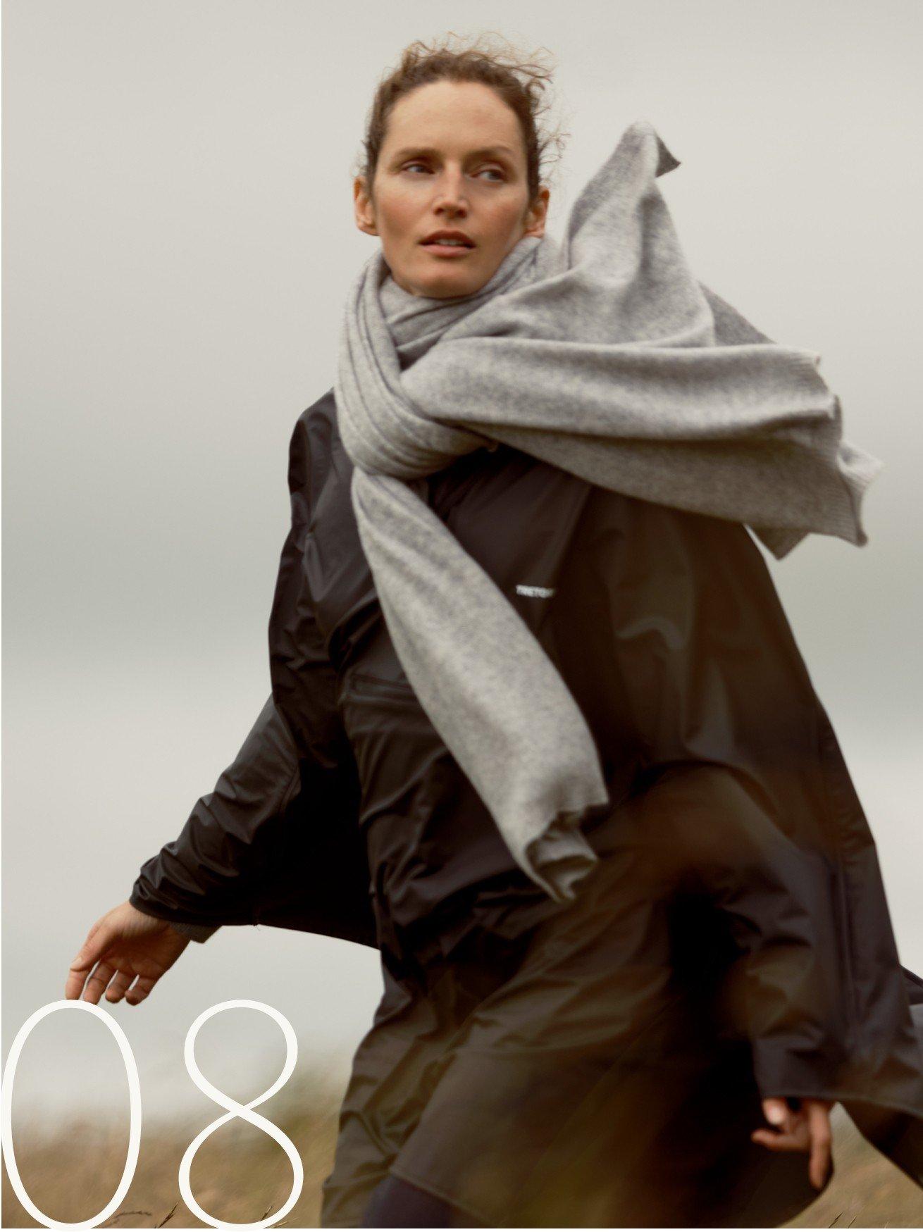 a woman walking in the field with a scarf wrapped around her