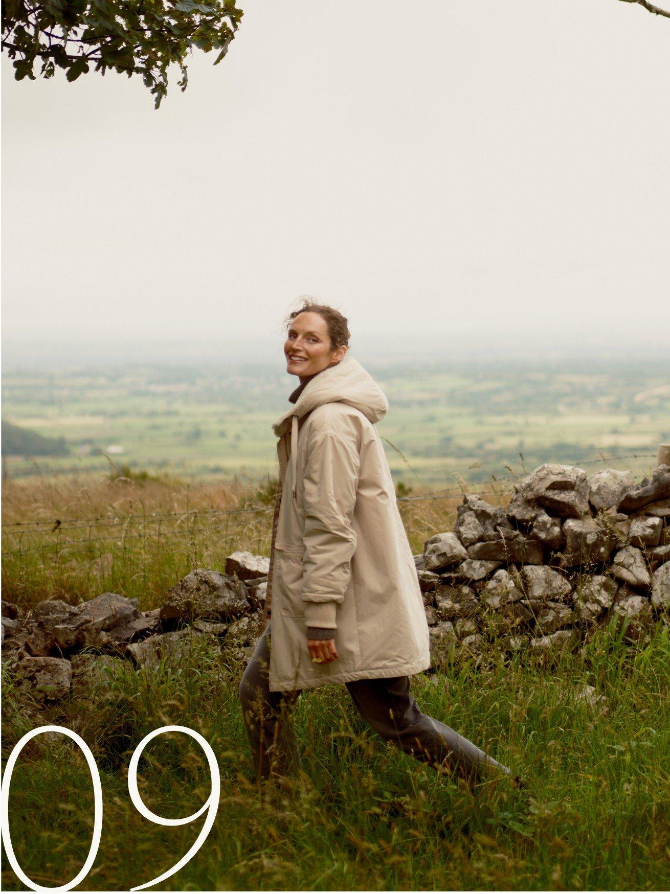 a woman walking in a field with a stone wall in the background