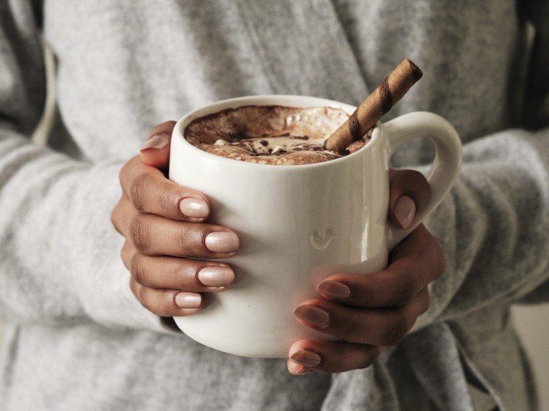 a person holding a cup of hot chocolate with a cinnamon stick