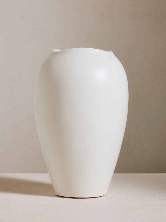 a white vase with a yellow dot on a white table