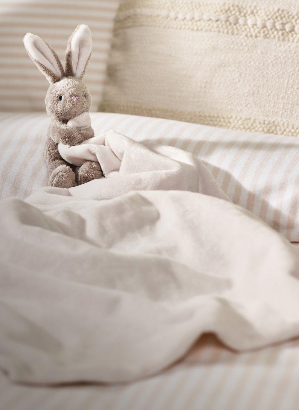 a stuffed rabbit sitting on top of a white bedspread