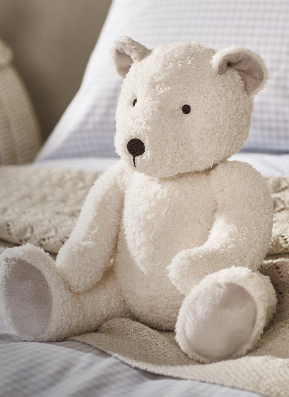 a white teddy bear sitting on a bed with a blanket