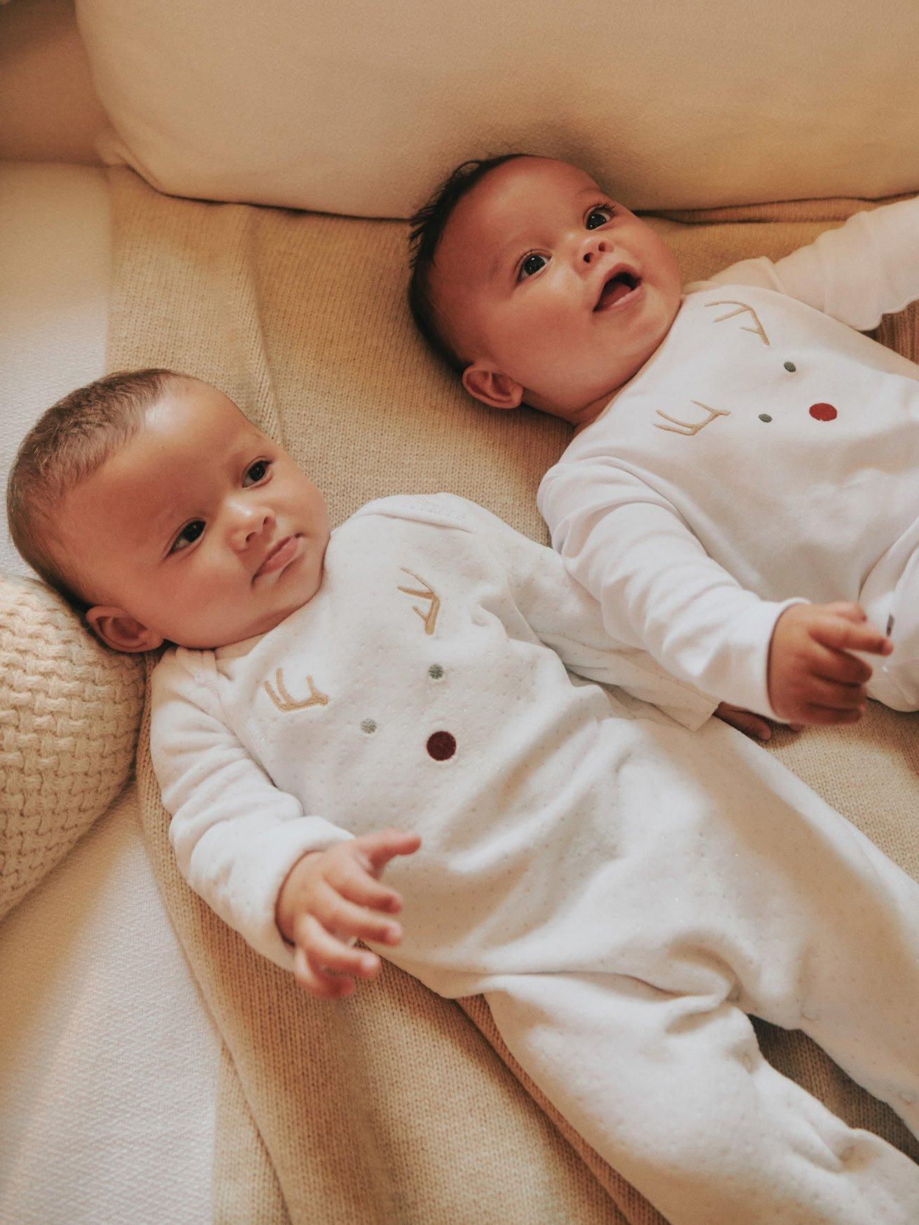 a baby in white pajamas laying on a bed