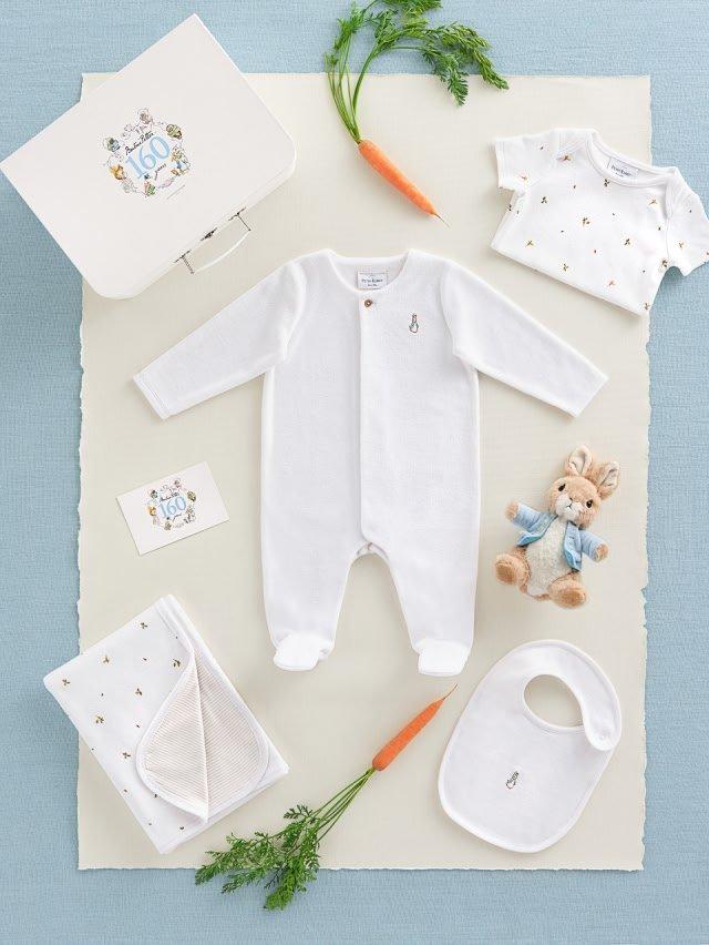 a baby's white outfit, a carrot, and a teddy bear