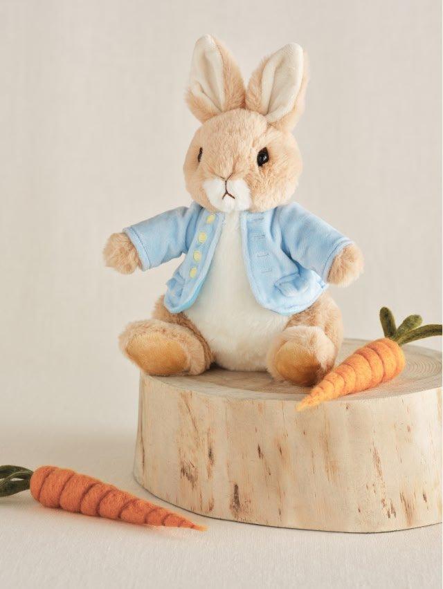 a stuffed rabbit sitting on a stump with two carrots