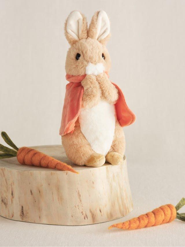 a small stuffed rabbit sitting on a stump with carrots