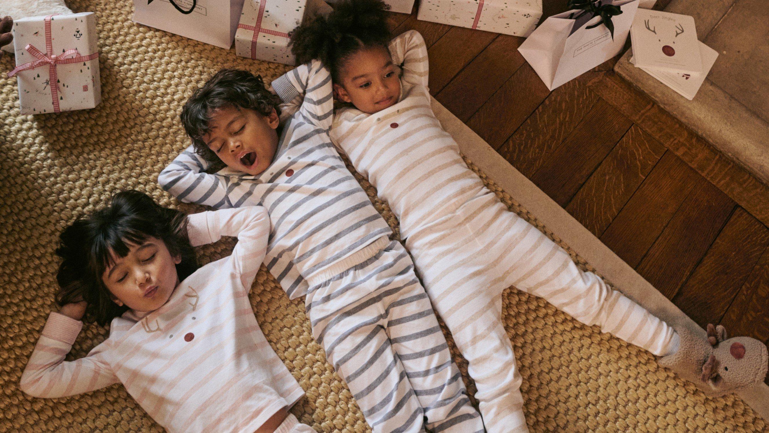 three children in pajamas laying on the floor next to presents