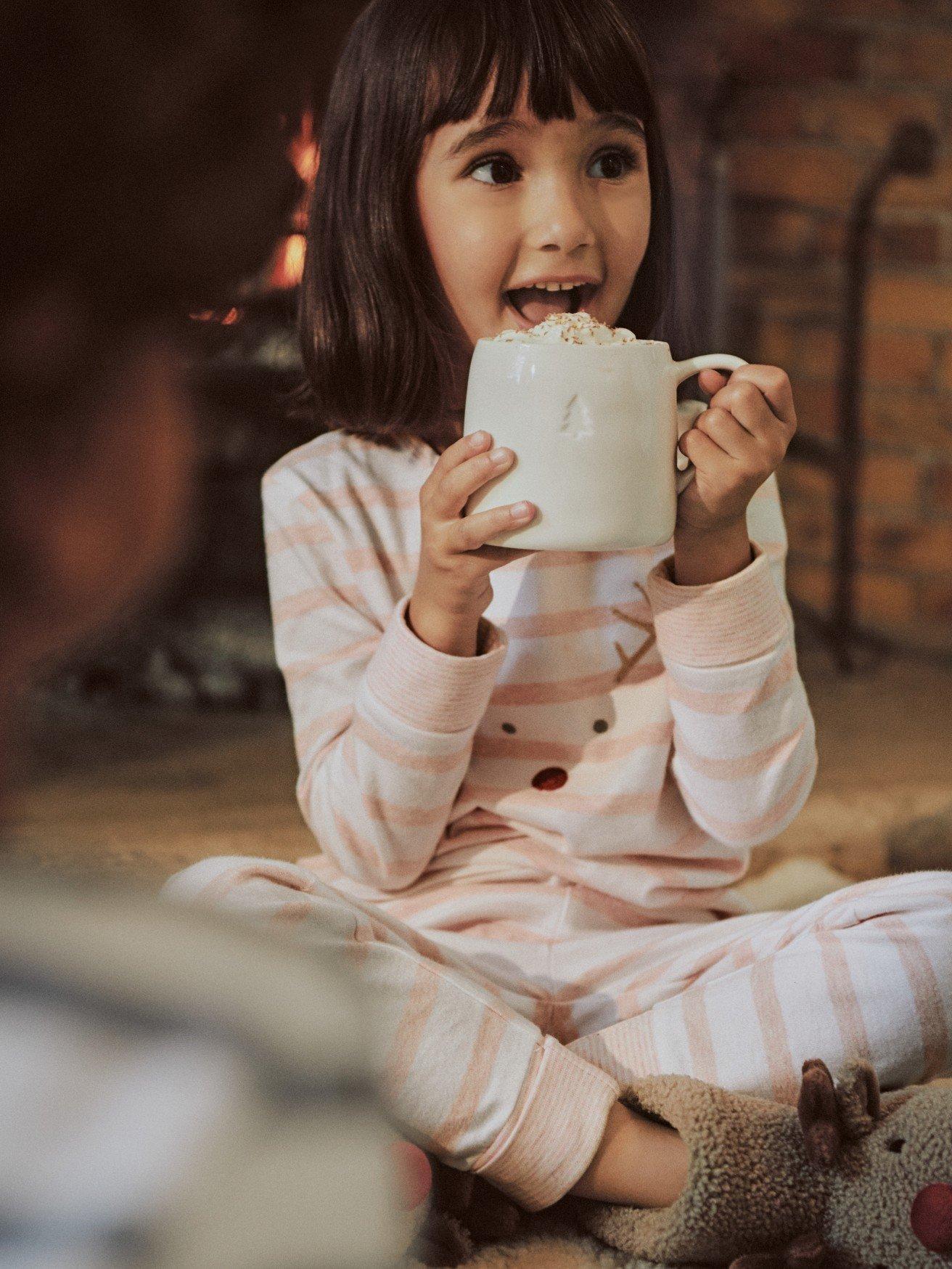 a little girl in pajamas holding a cup of hot chocolate