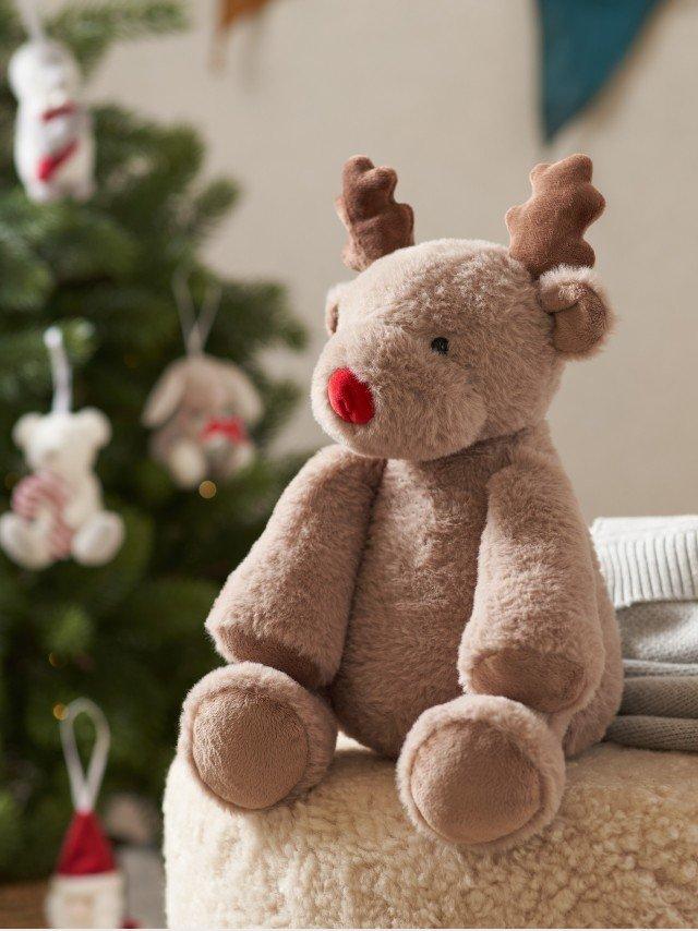 a stuffed reindeer sitting on a stool next to a christmas tree