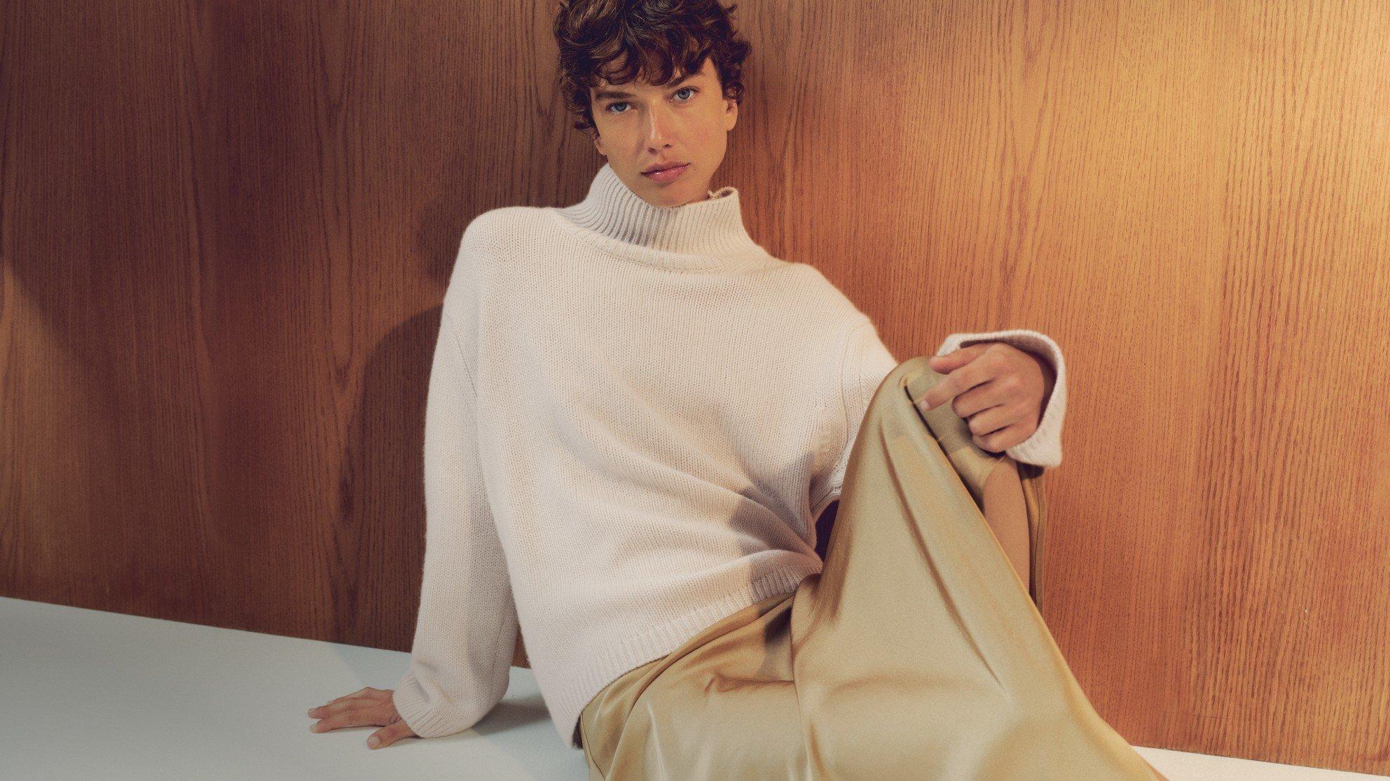 a man in a white sweater and tan pants sitting on a table