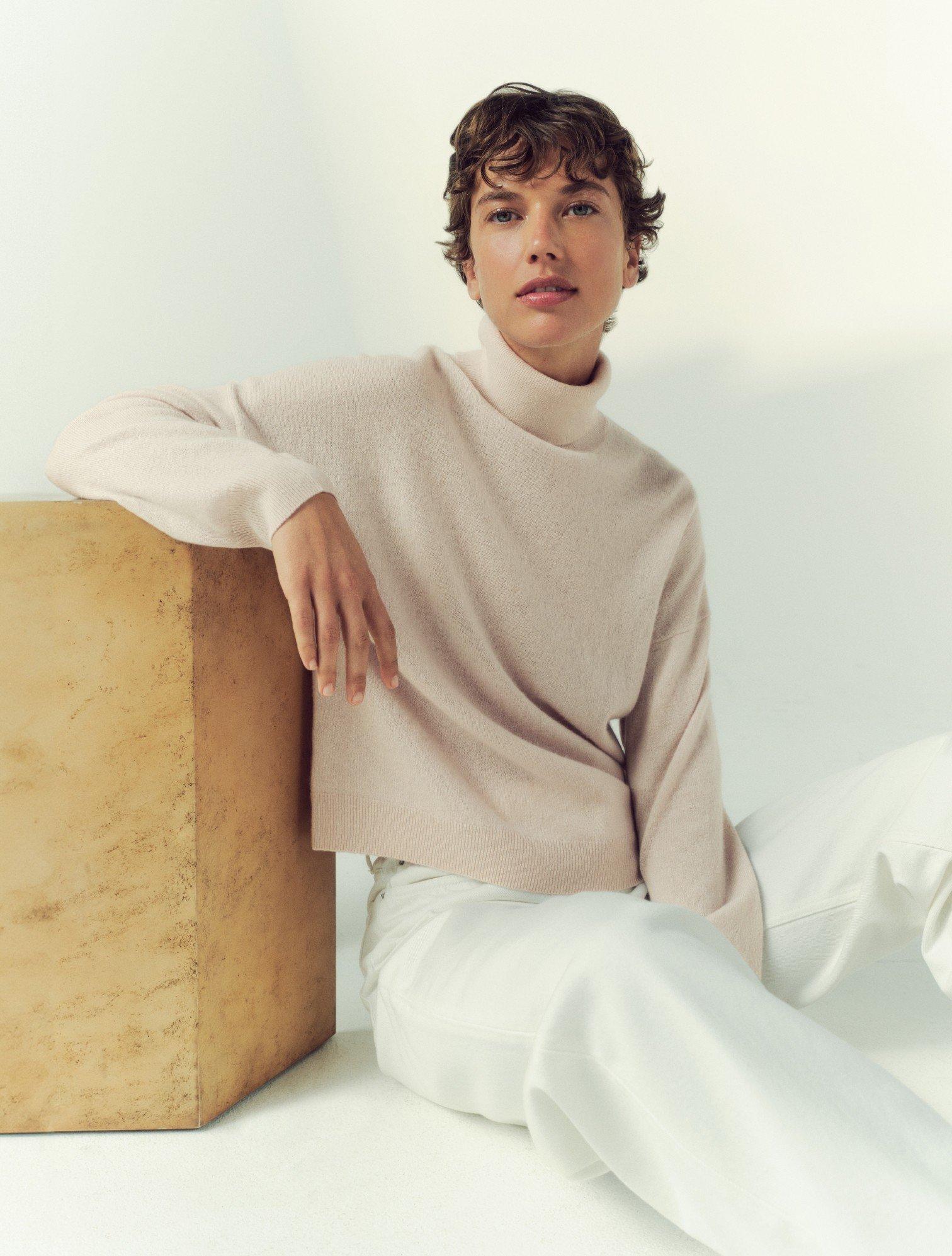 a woman in a white sweater sitting on a wooden box