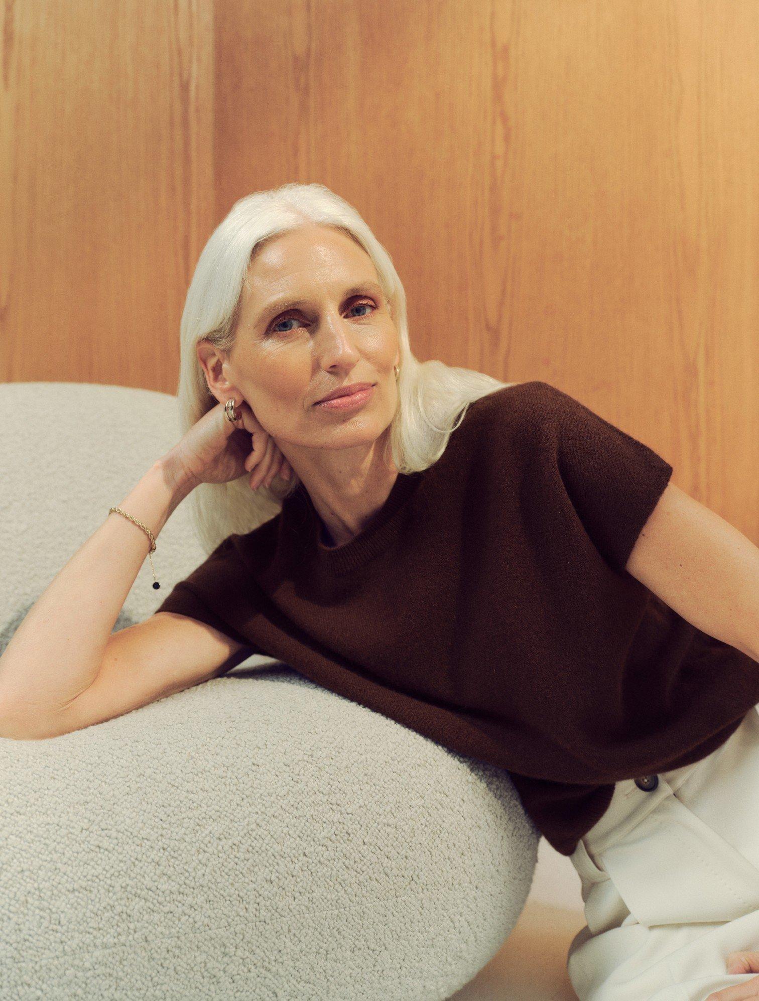 a woman with white hair sitting on a couch with her hand on her chin