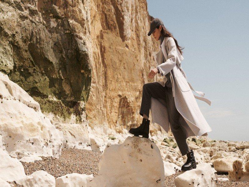 a woman in a long coat walking on a rock near a cliff