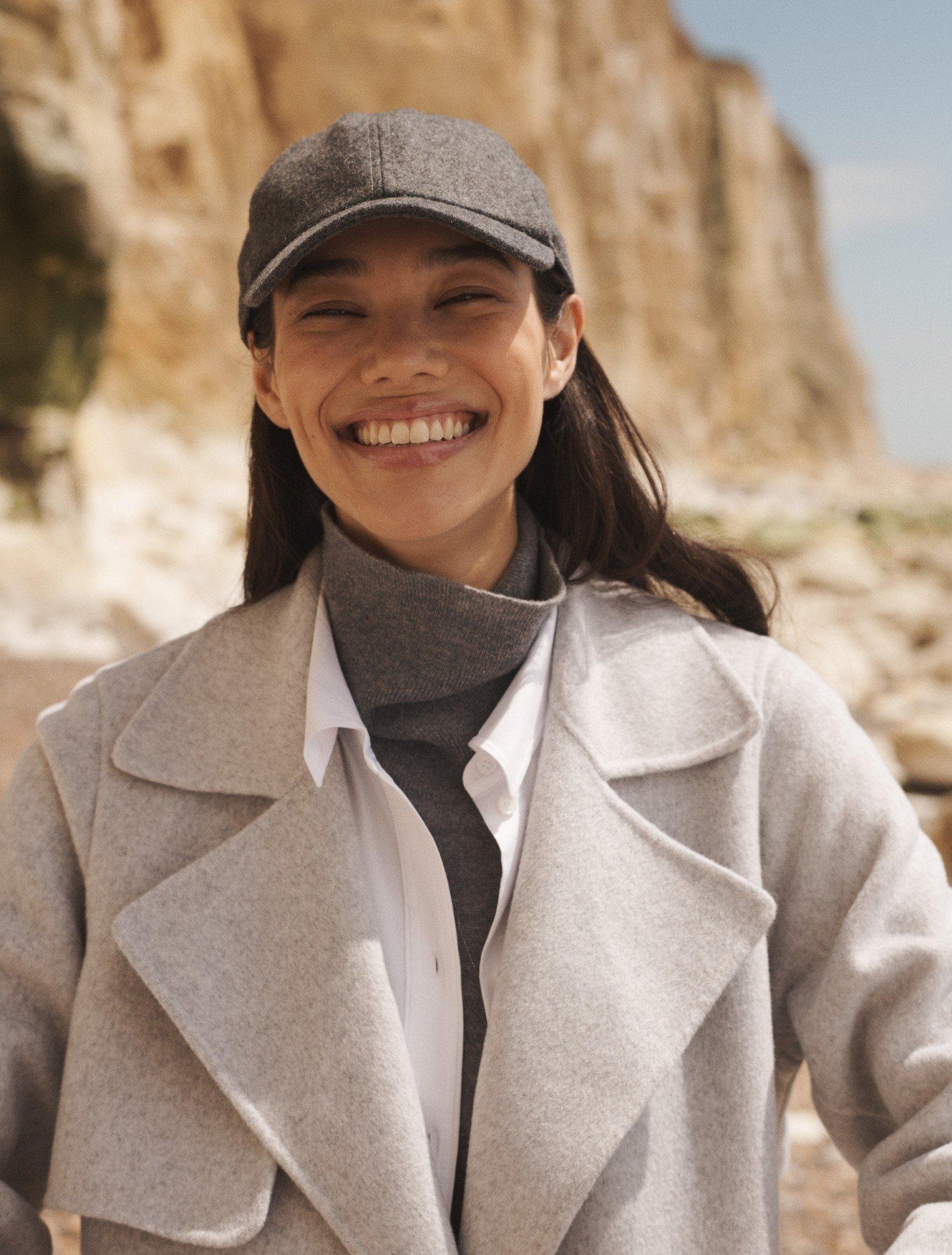 a woman in a gray coat and hat smiling at the camera