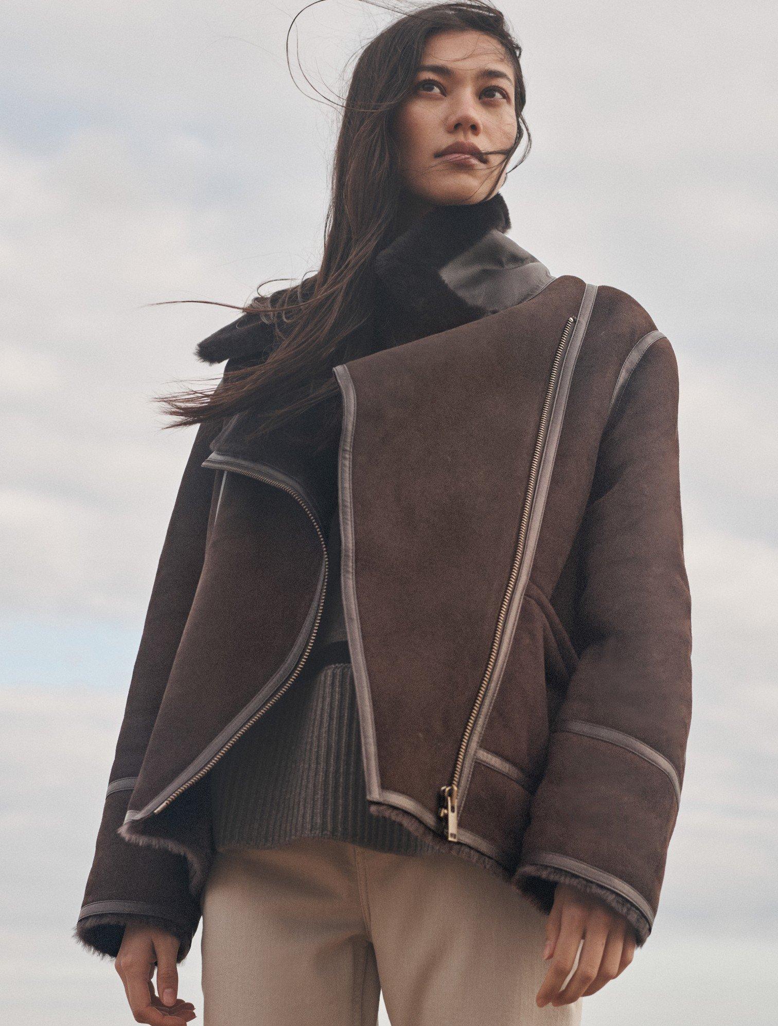 a woman standing in a field wearing a jacket and pants