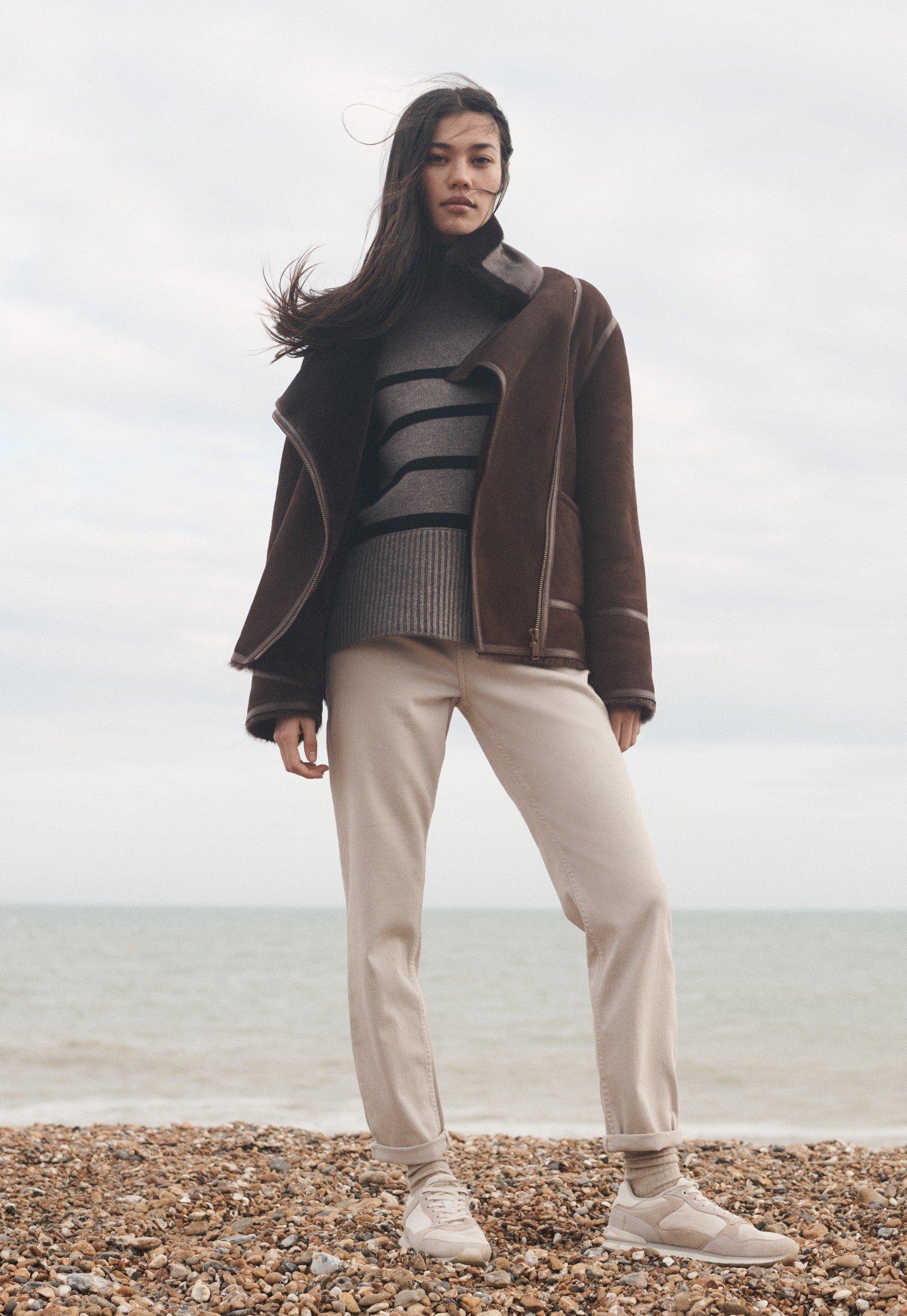 a woman standing on a beach wearing a jacket and pants