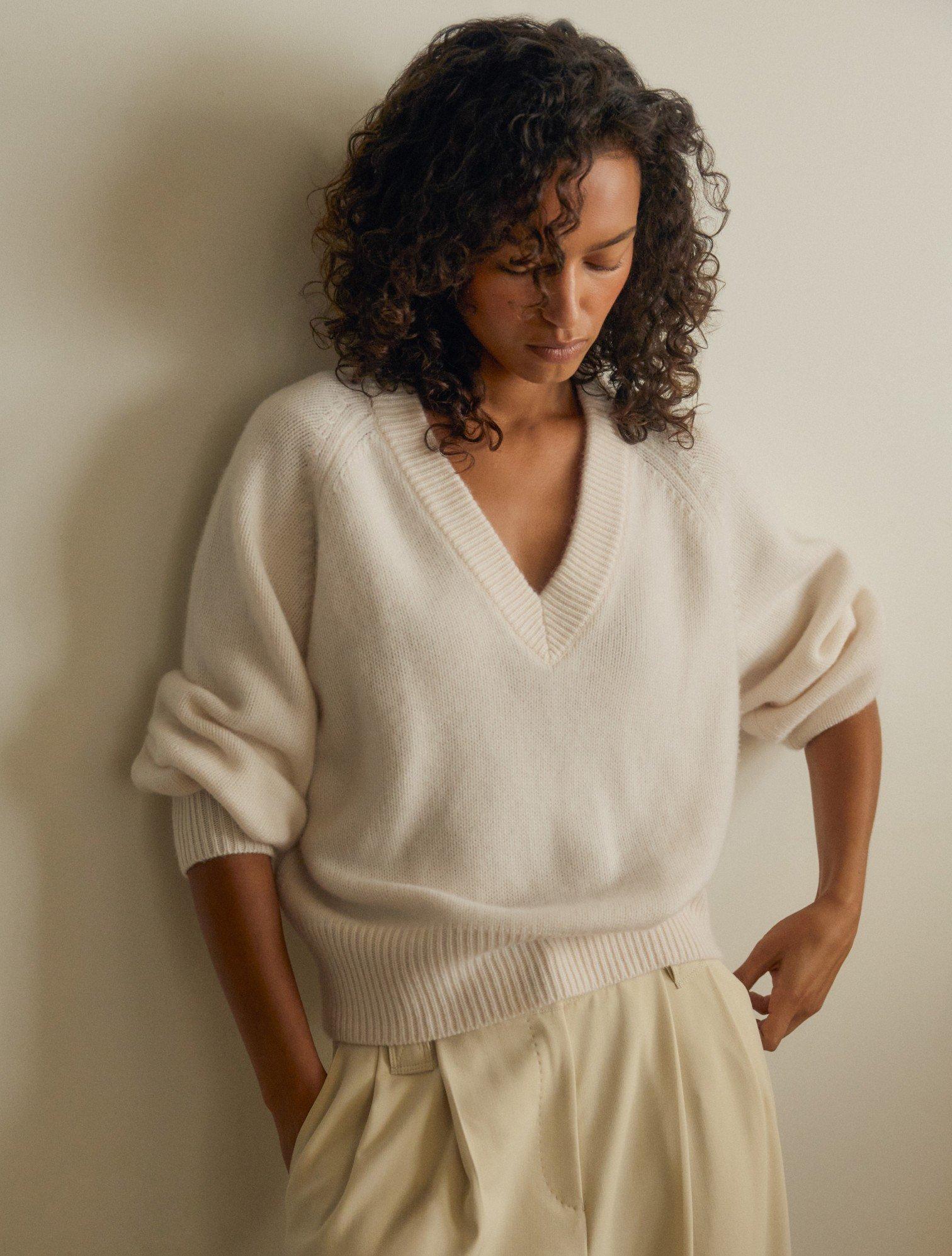 a woman in a white sweater leaning against a wall