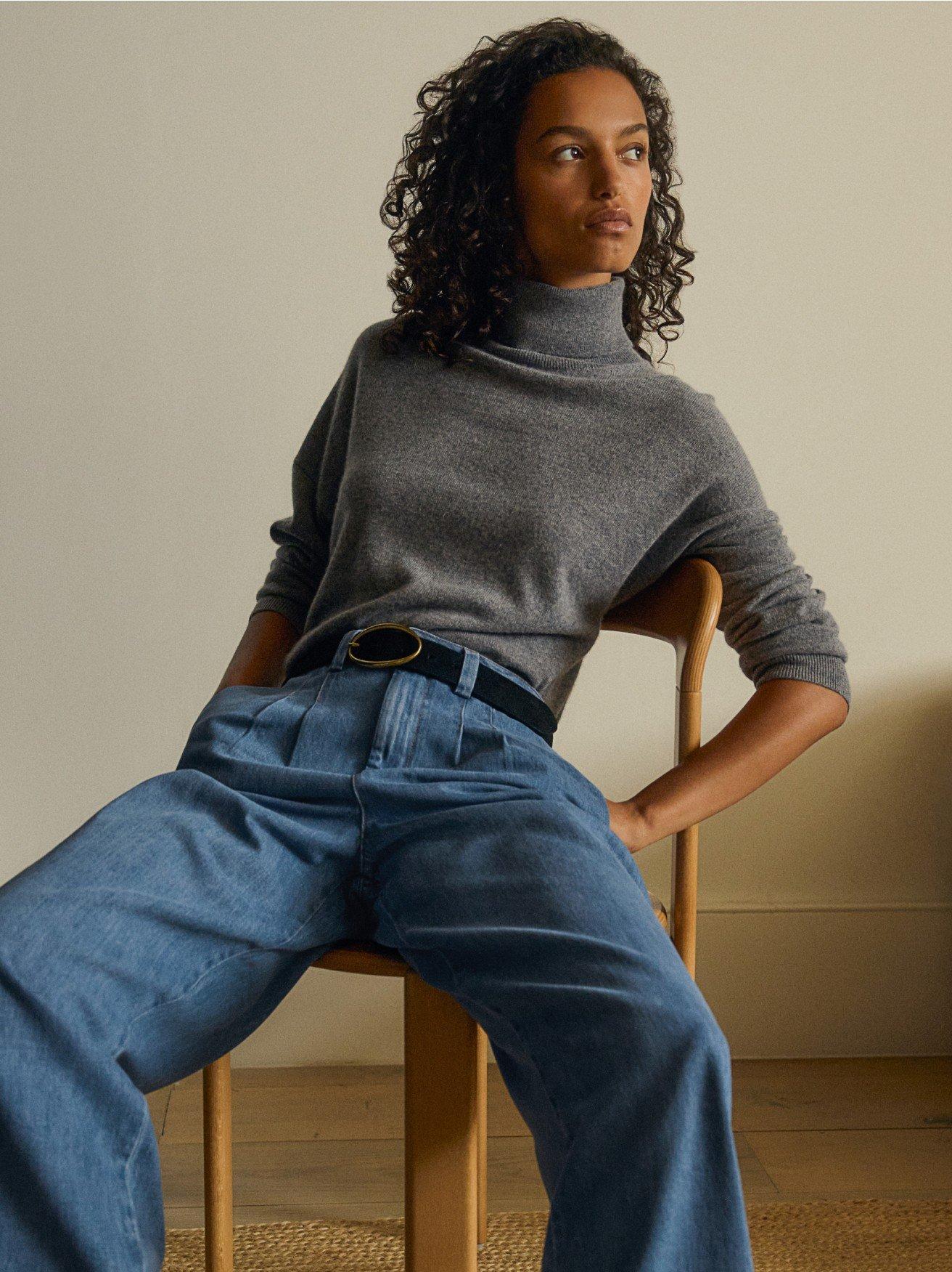 a woman in a grey sweater and a pleated skirt holding a sweater