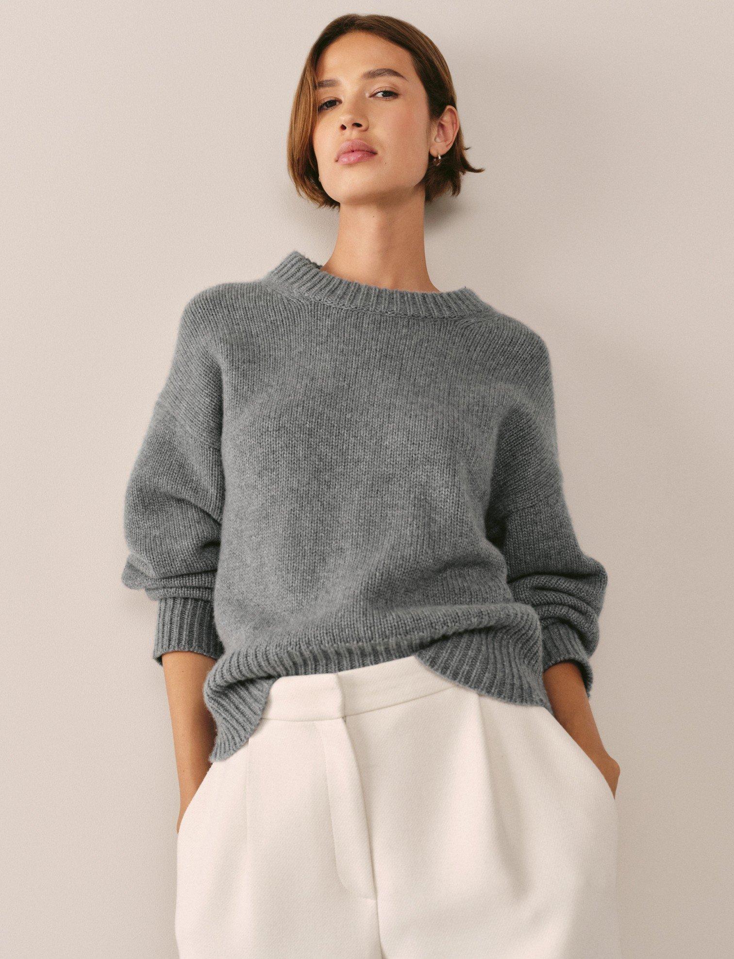 a woman in a grey sweater and white pants posing for a picture
