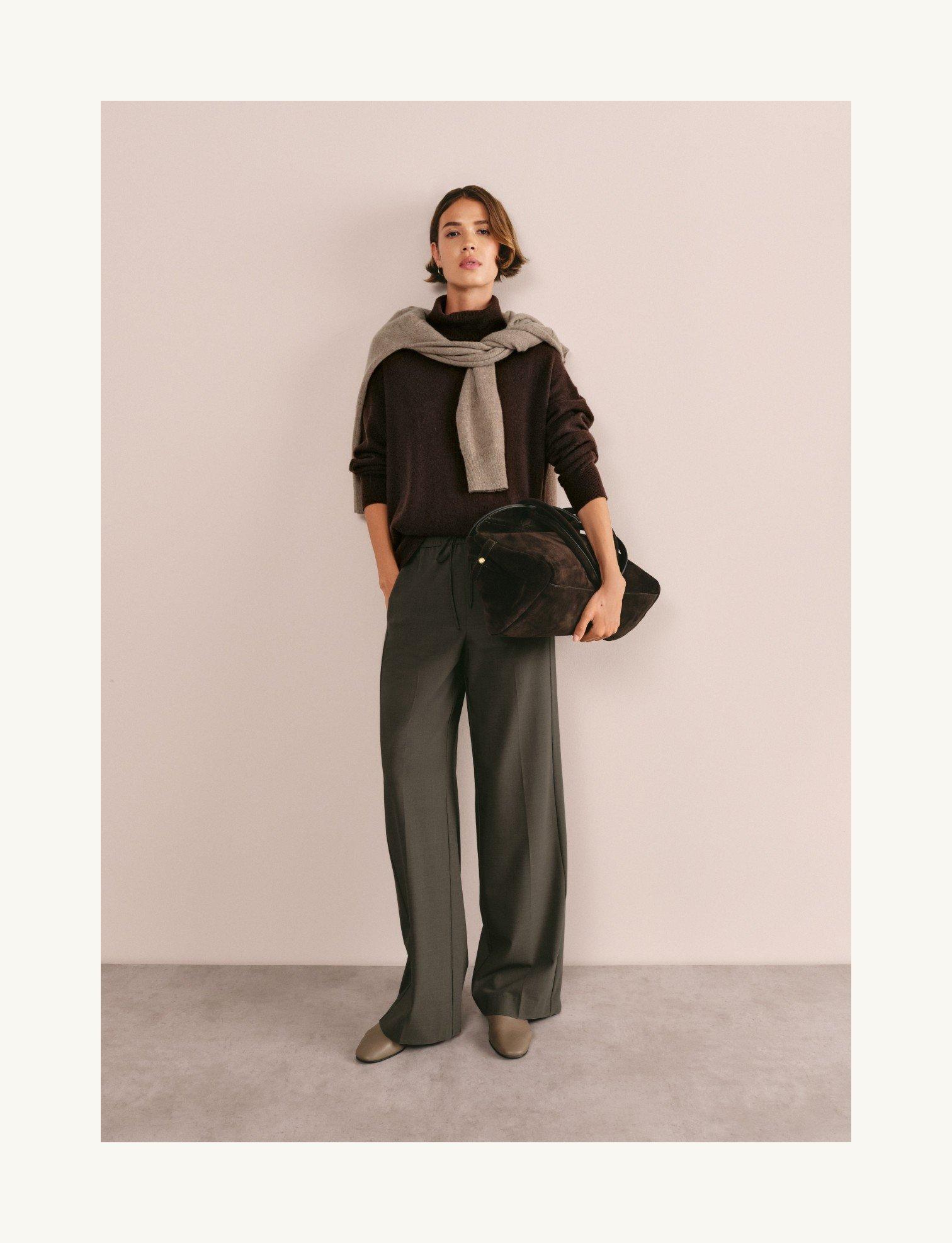 a woman in a sweater and pants holding a bag