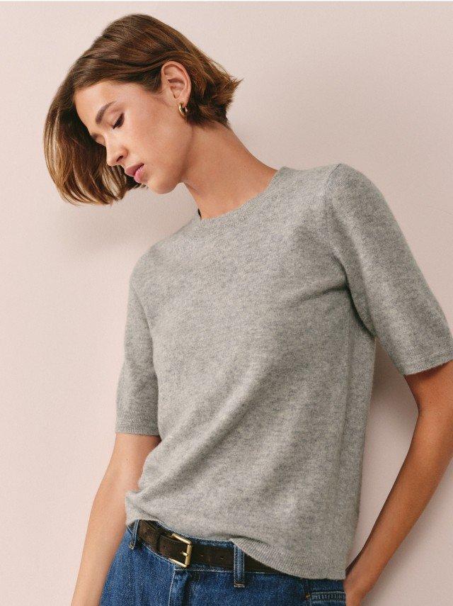 a woman in a grey t shirt and jeans leaning against a wall