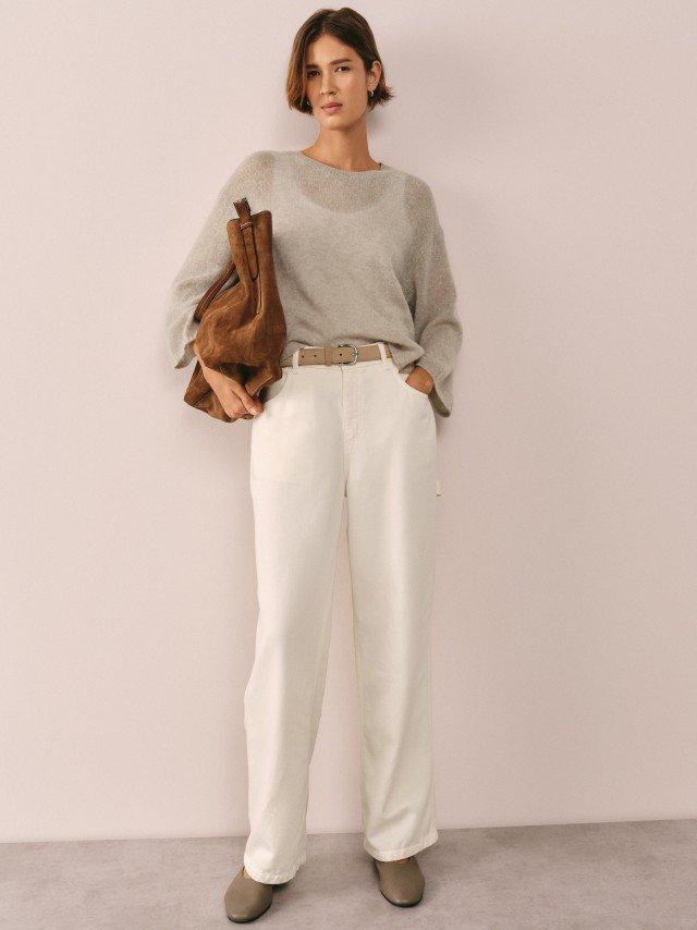 a woman in a grey sweater and white pants holding a yellow bag