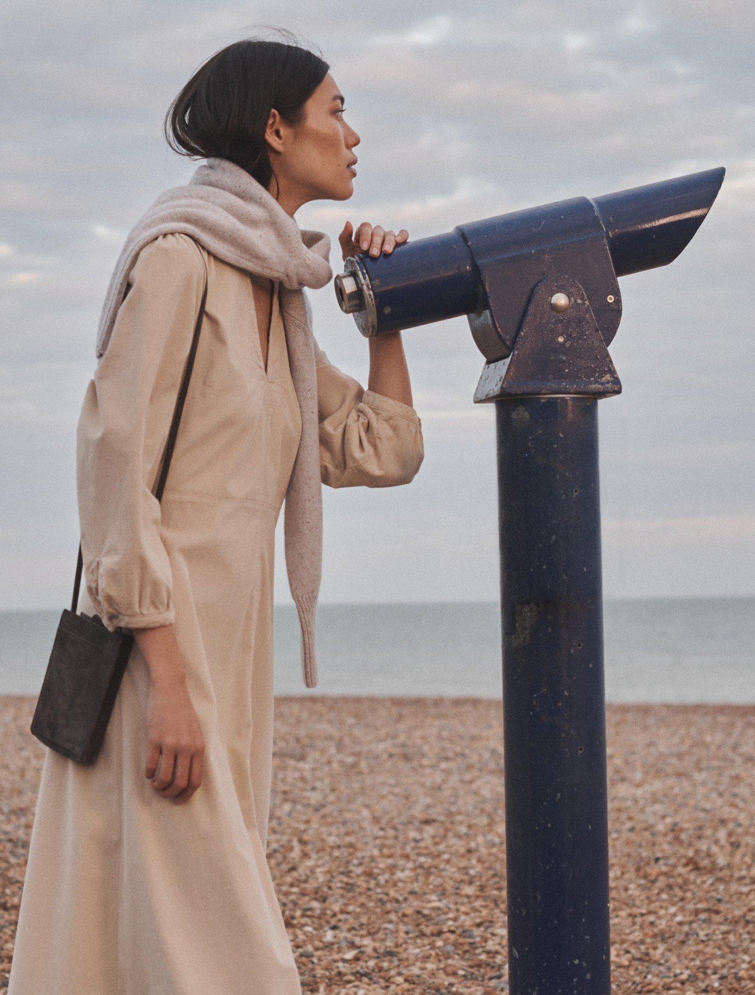 a woman posing next to a telescope at the beach