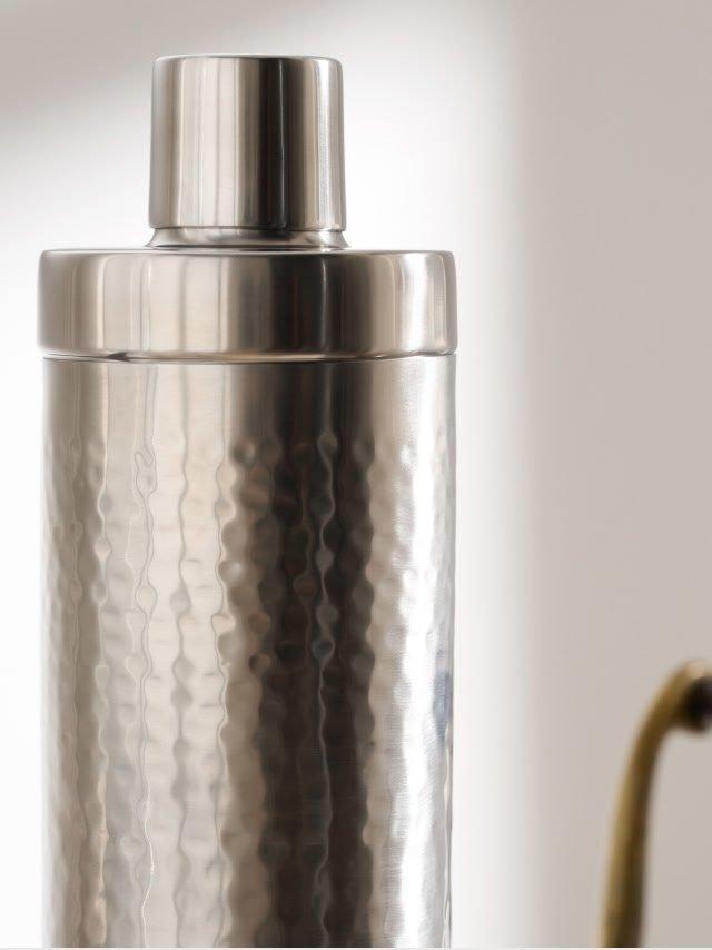 a metal cocktail shaker with a straw and a metal spoon