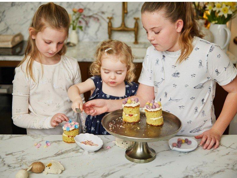 three young girls are making small cakes on a table