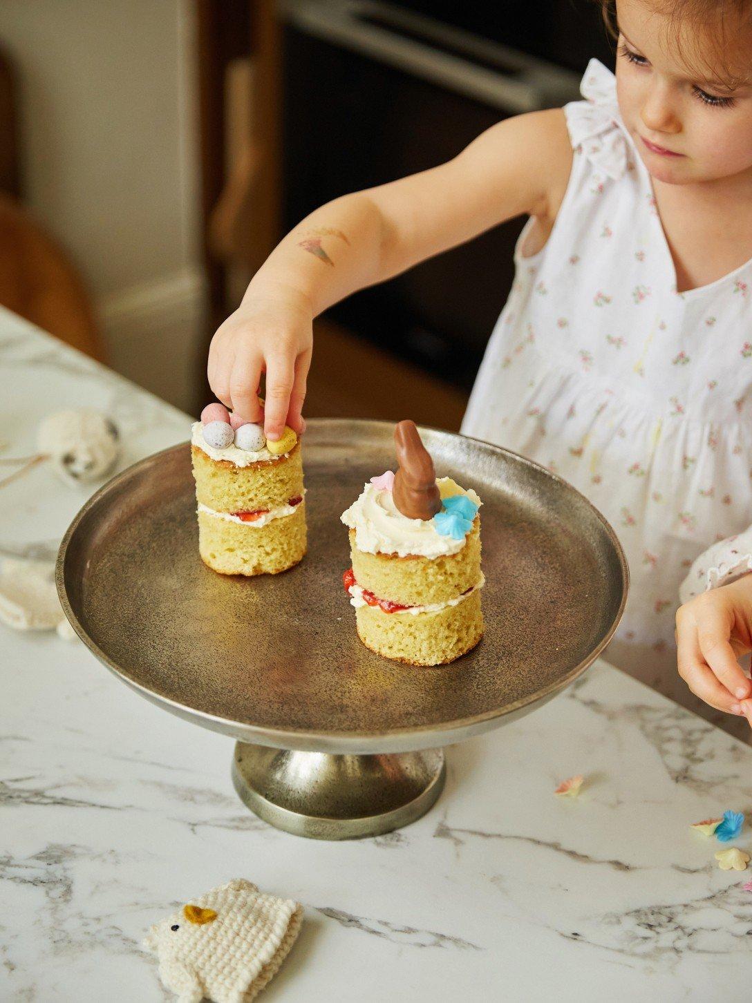 a little girl is putting a small cake on a plate