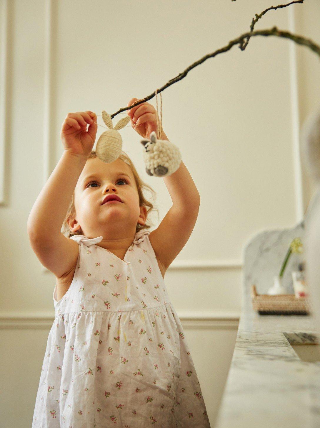 a little girl in a dress holding a branch with a bird on it