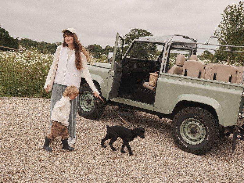 a woman and child walking a dog in front of a green jeep