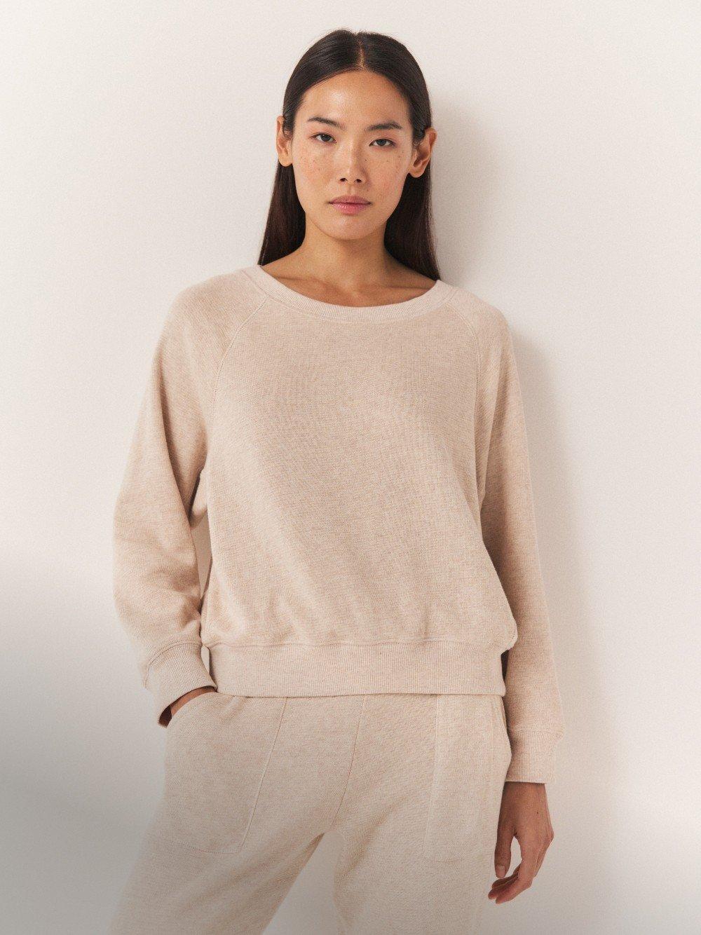 a woman in a beige sweater and matching pants standing against a white wall