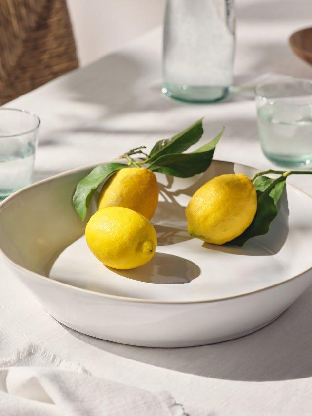 a bowl of lemons on a table with two glasses of water