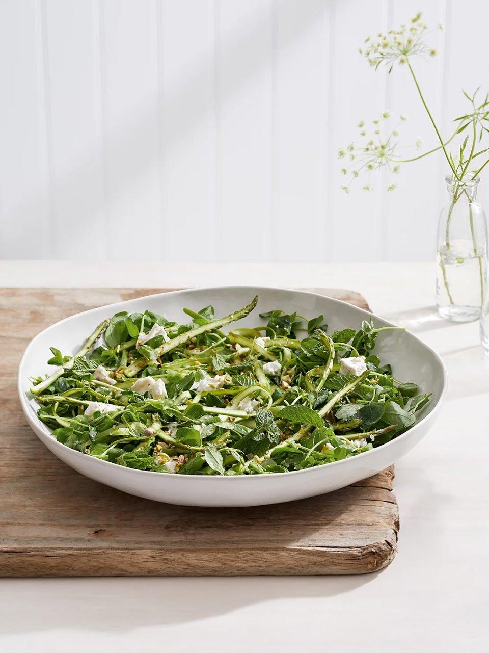 a white bowl filled with green salad on a wooden cutting board