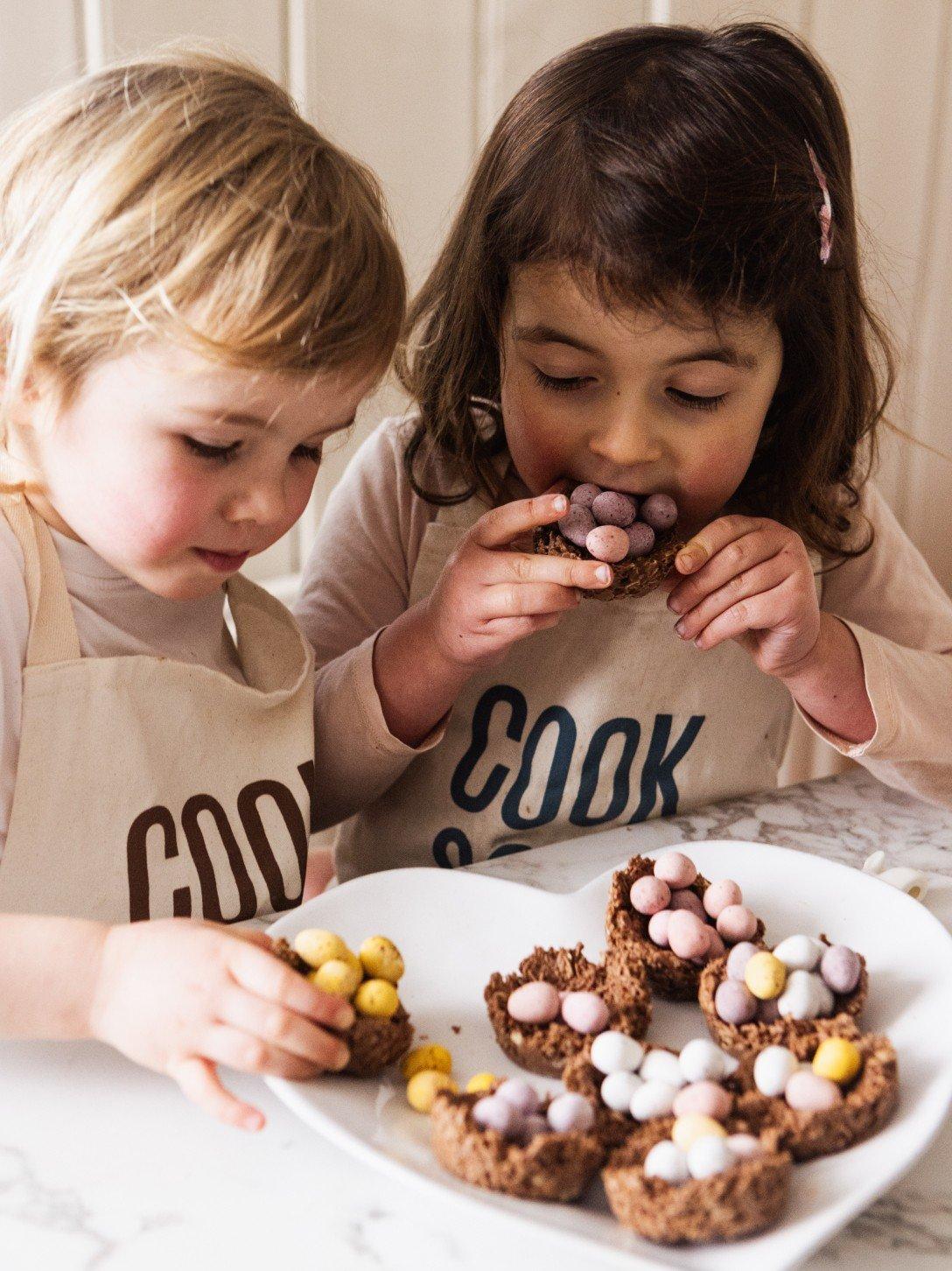 two young girls in pajamas eating pastries in front of a christmas tree
