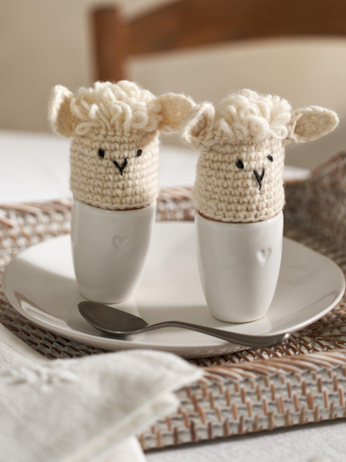 two crocheted sheep are sitting on a plate with a spoon