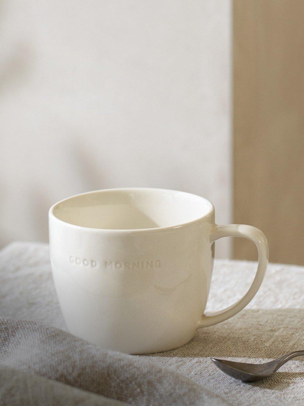 a white cup with a spoon sitting on a table