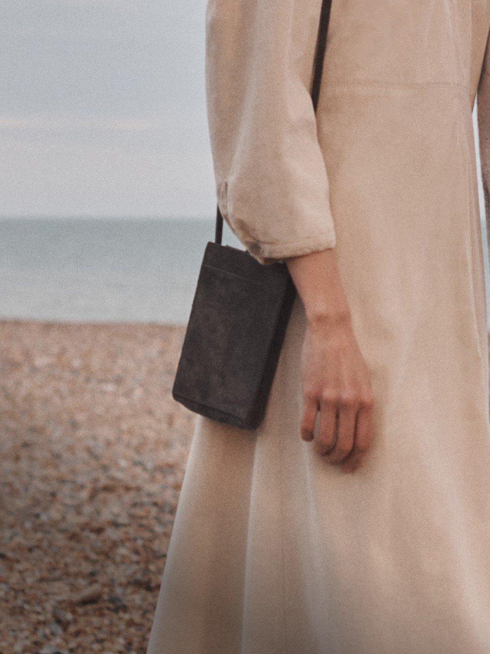 a woman in a long dress walking on a beach with a purse