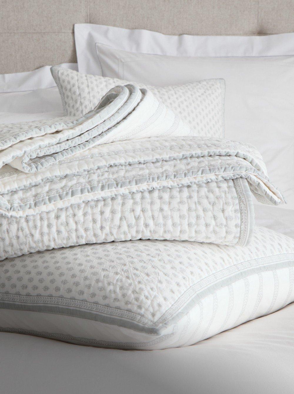 a pile of pillows on a bed with a white comforter