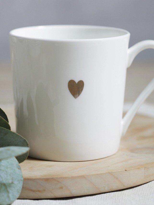 a white cup with a heart on it sitting on a wooden board