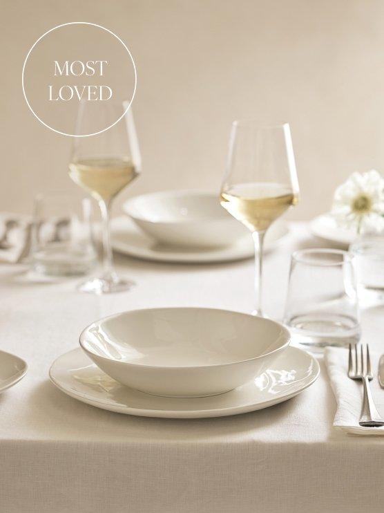 a white table set with white plates and glasses and a white napkin